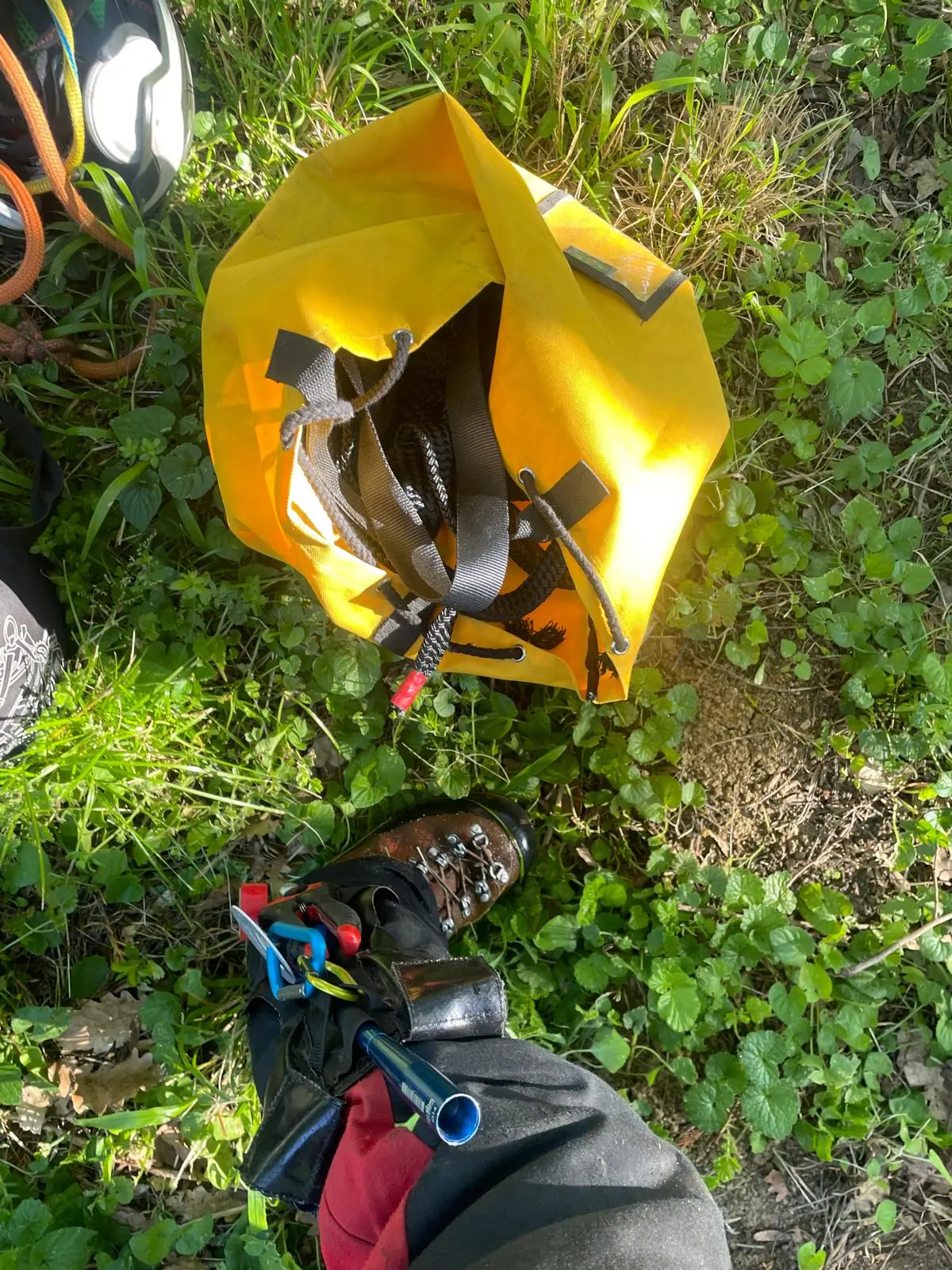 Sac jaune ouvert posé dans l’herbe, et une chaussure de grimpe avec son porte-outils au mollet